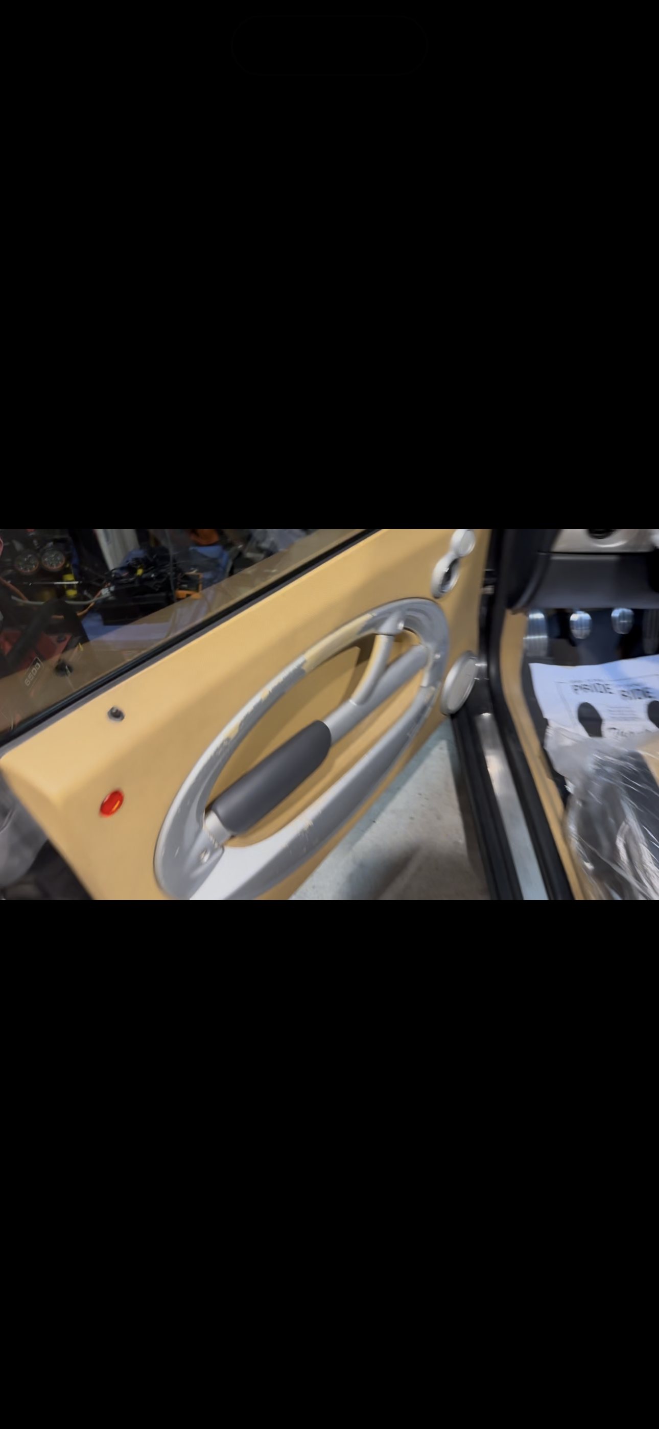 Open driver door of a first-generation MINI Cooper with the tan interior door panel and oval pull handle visible