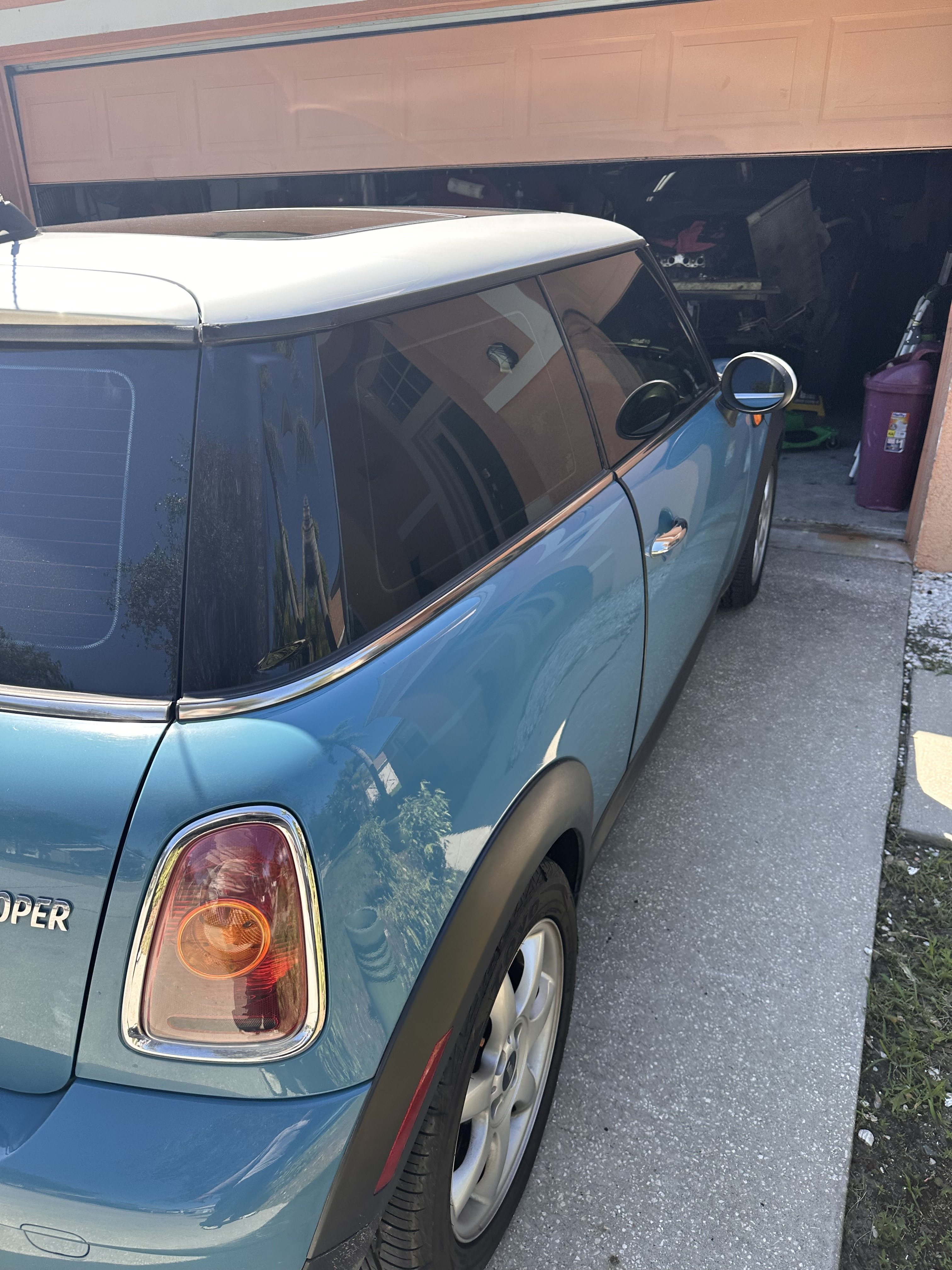 Rear quarter and passenger side of the blue MINI Clubman with a white roof, parked by a garage
