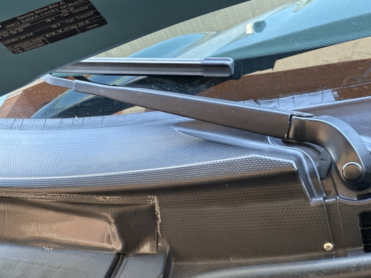 Windshield cowl trim below a wiper arm, cracked with a section of plastic missing
