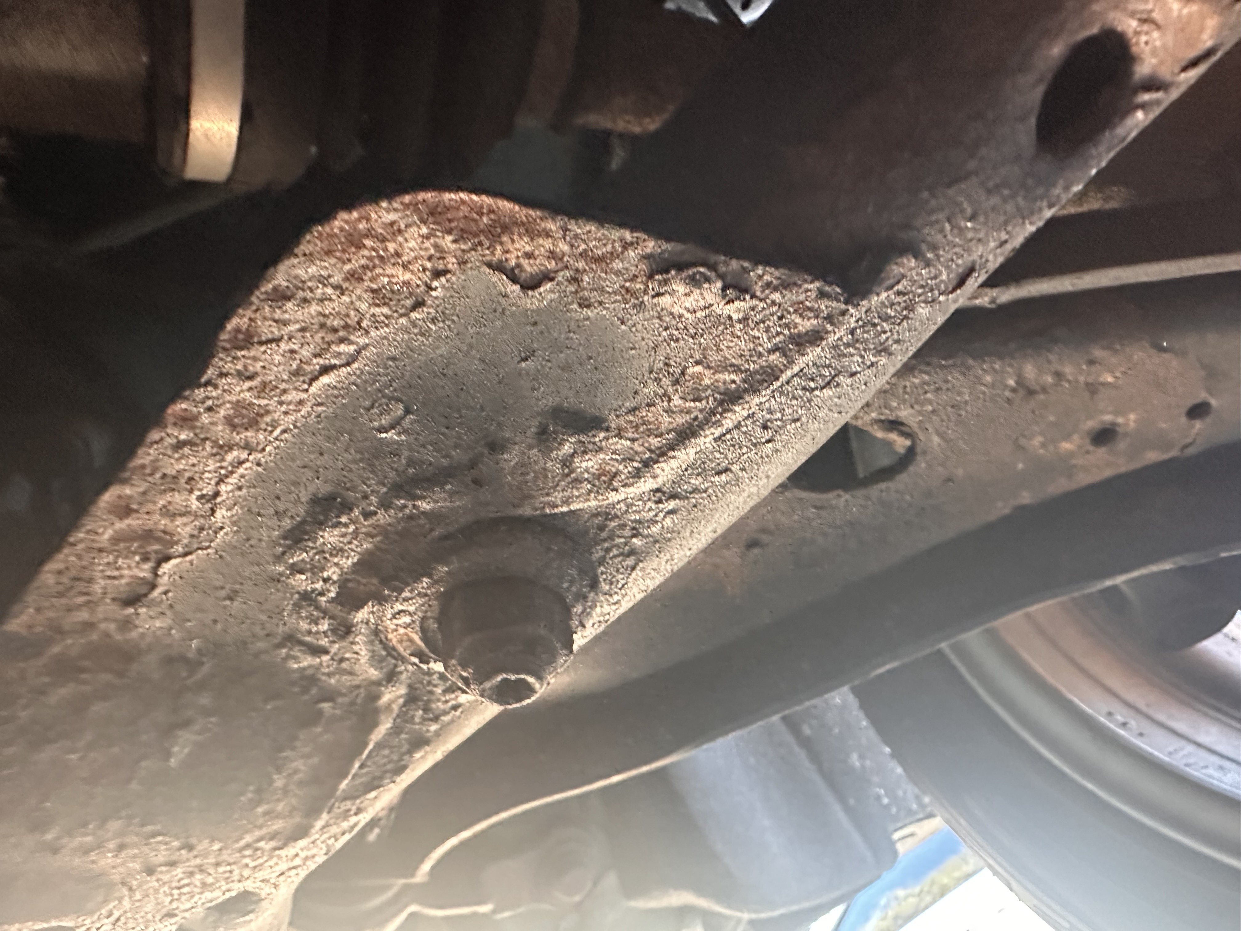 Rust-covered steel underbody member around a mounting bolt, seen from beneath the car