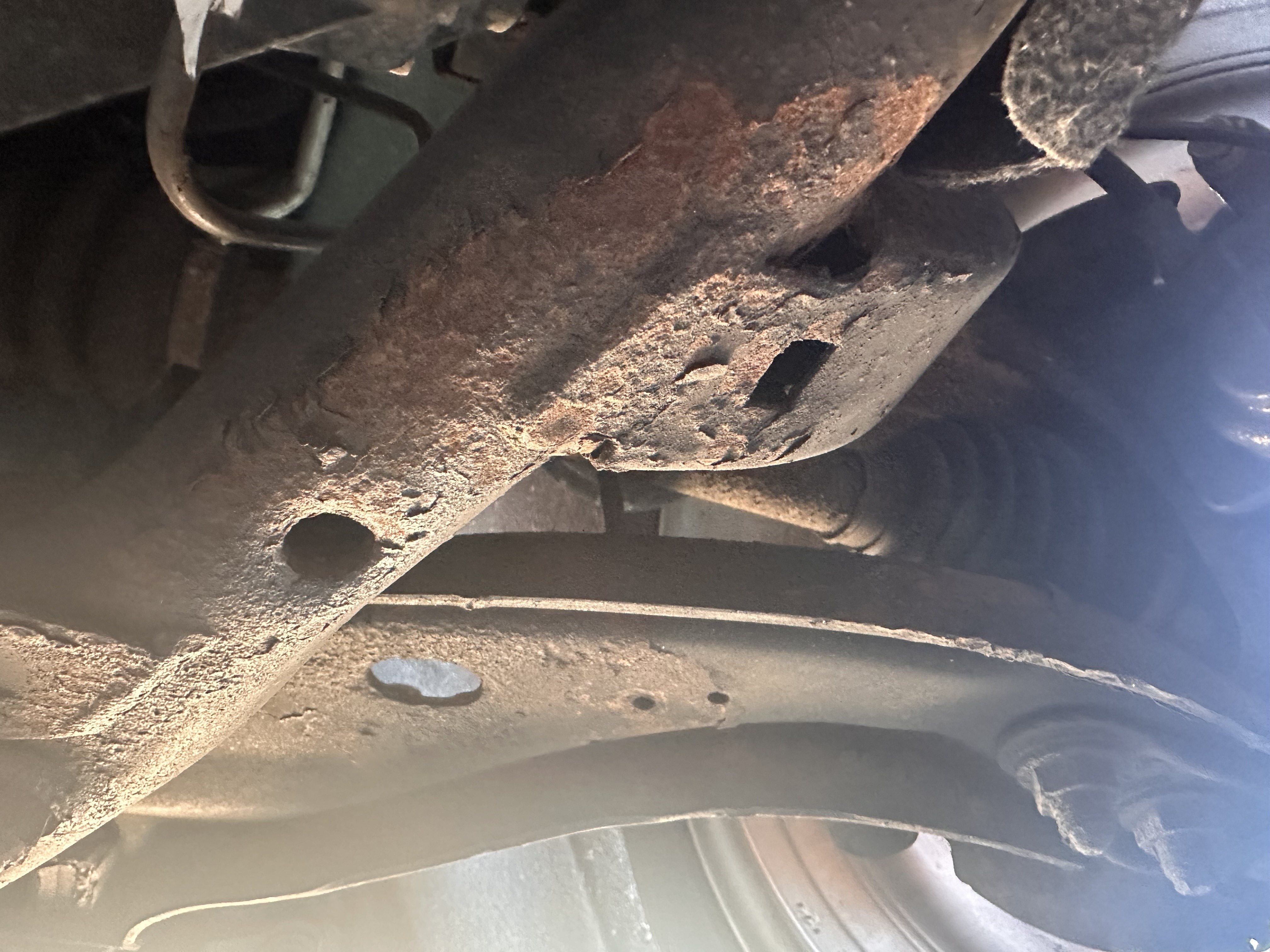 Rusted underbody steel near the front suspension, with a CV boot visible behind