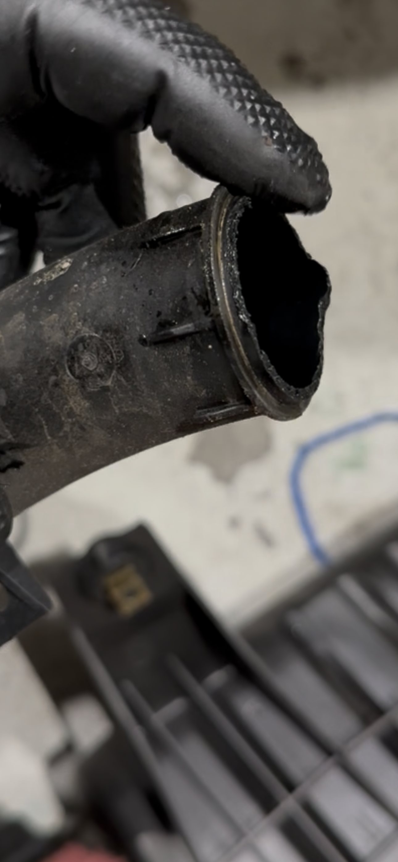 The removed coolant crossover pipe held over a workshop bench, showing its curved body and mounting tab alongside the damaged end
