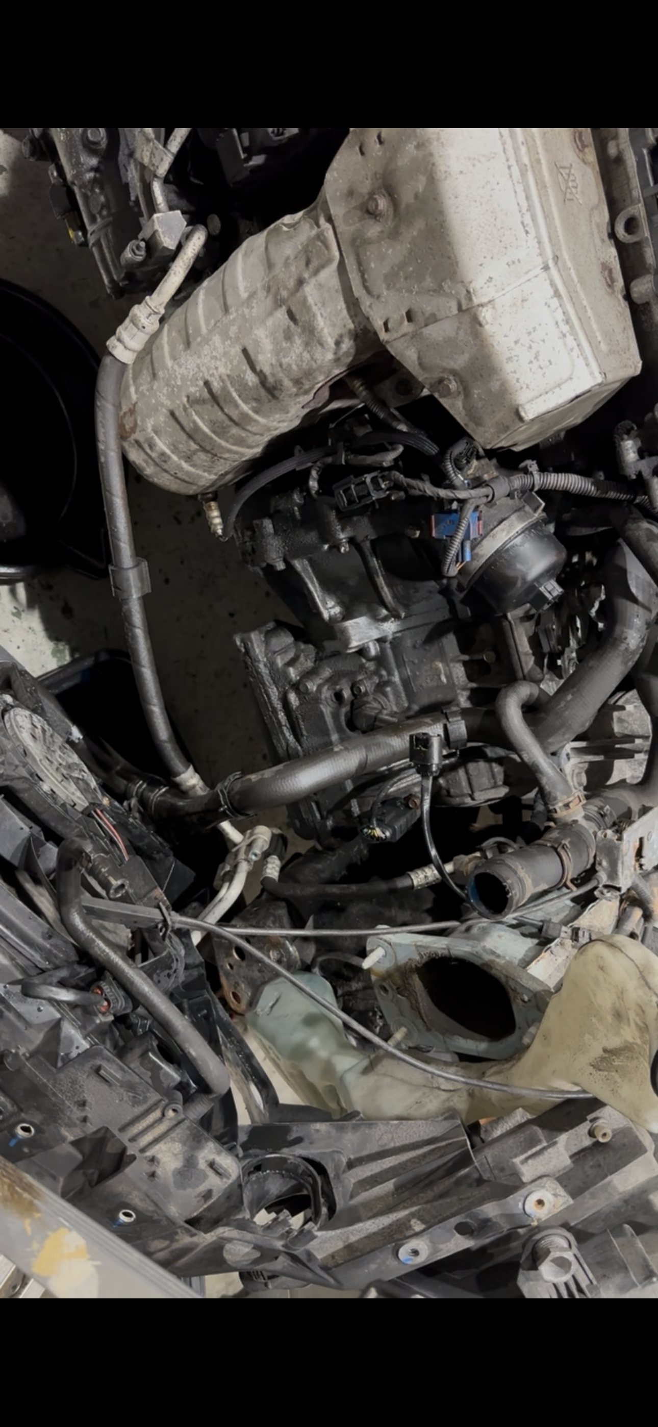 Front of the 1.6-litre engine exposed with the bumper and cooling pack out of the way, showing the oil filter housing area, its coolant hoses and the exhaust above it