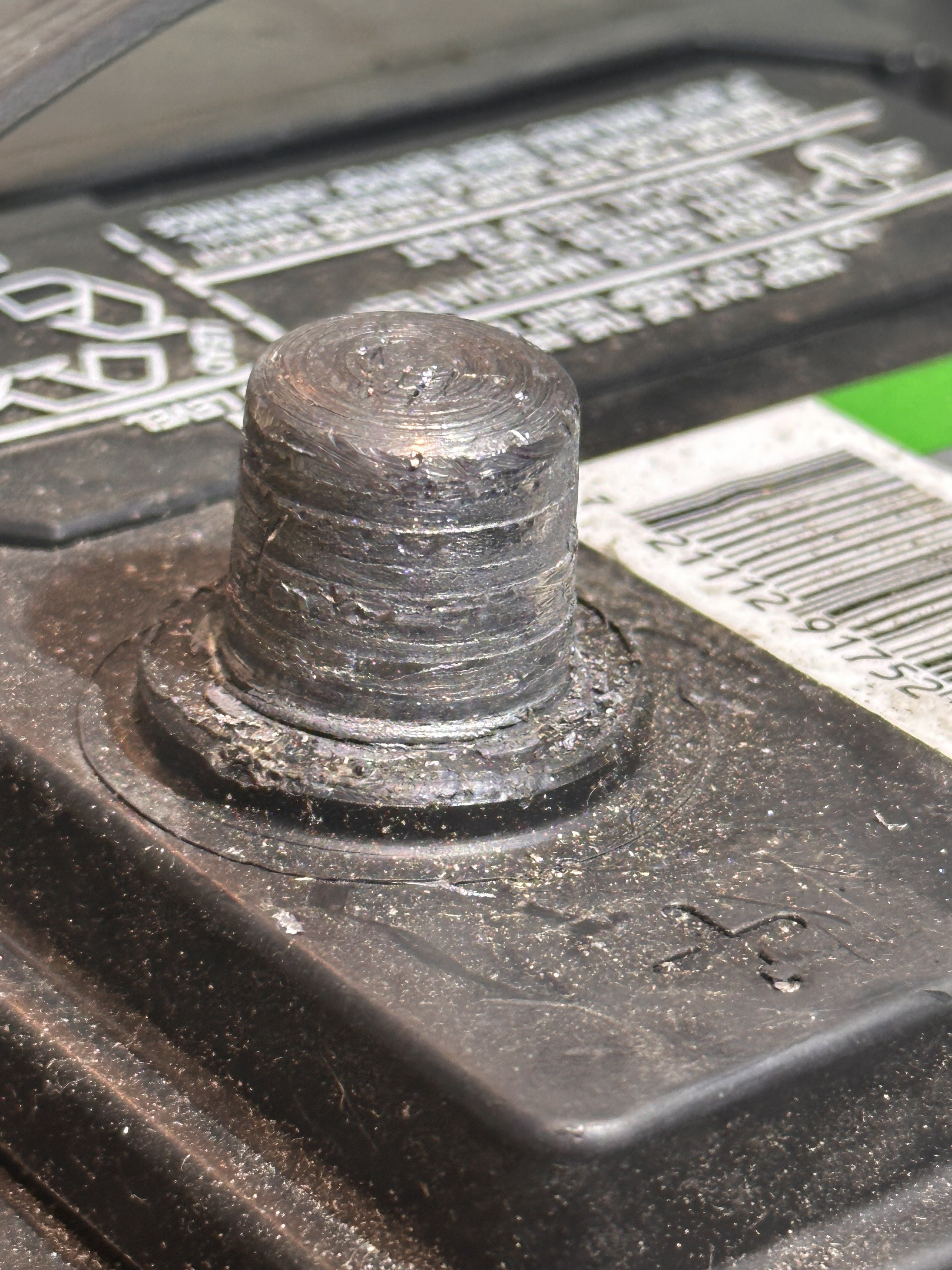 Battery post before cleaning, with a shiny but scored and pitted surface and debris packed on the ledge at its base.