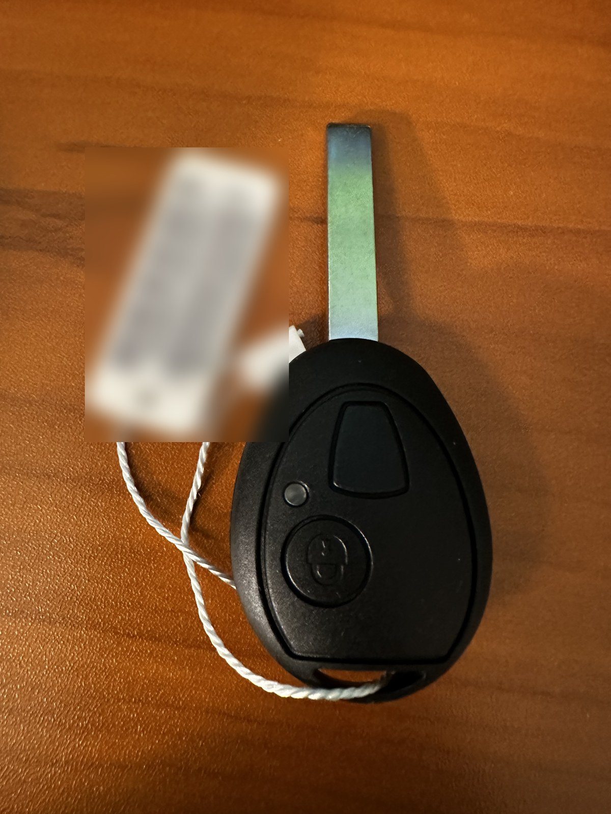 First-generation MINI key with an oval two-button head and a flat metal blade, its shop tag deliberately blurred