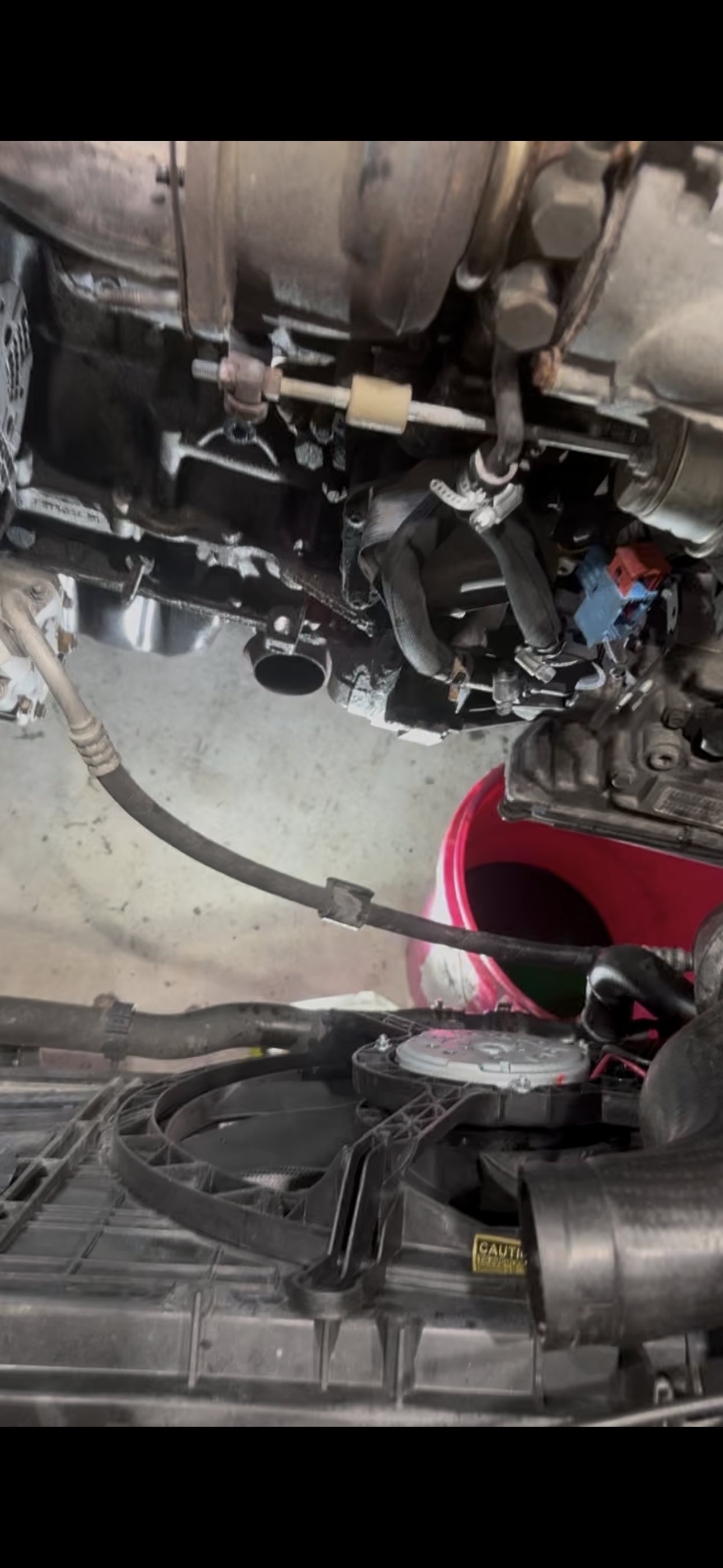 View from under the raised MINI showing the exhaust and turbocharger area of the engine with hoses and connectors disconnected above the cooling fan assembly