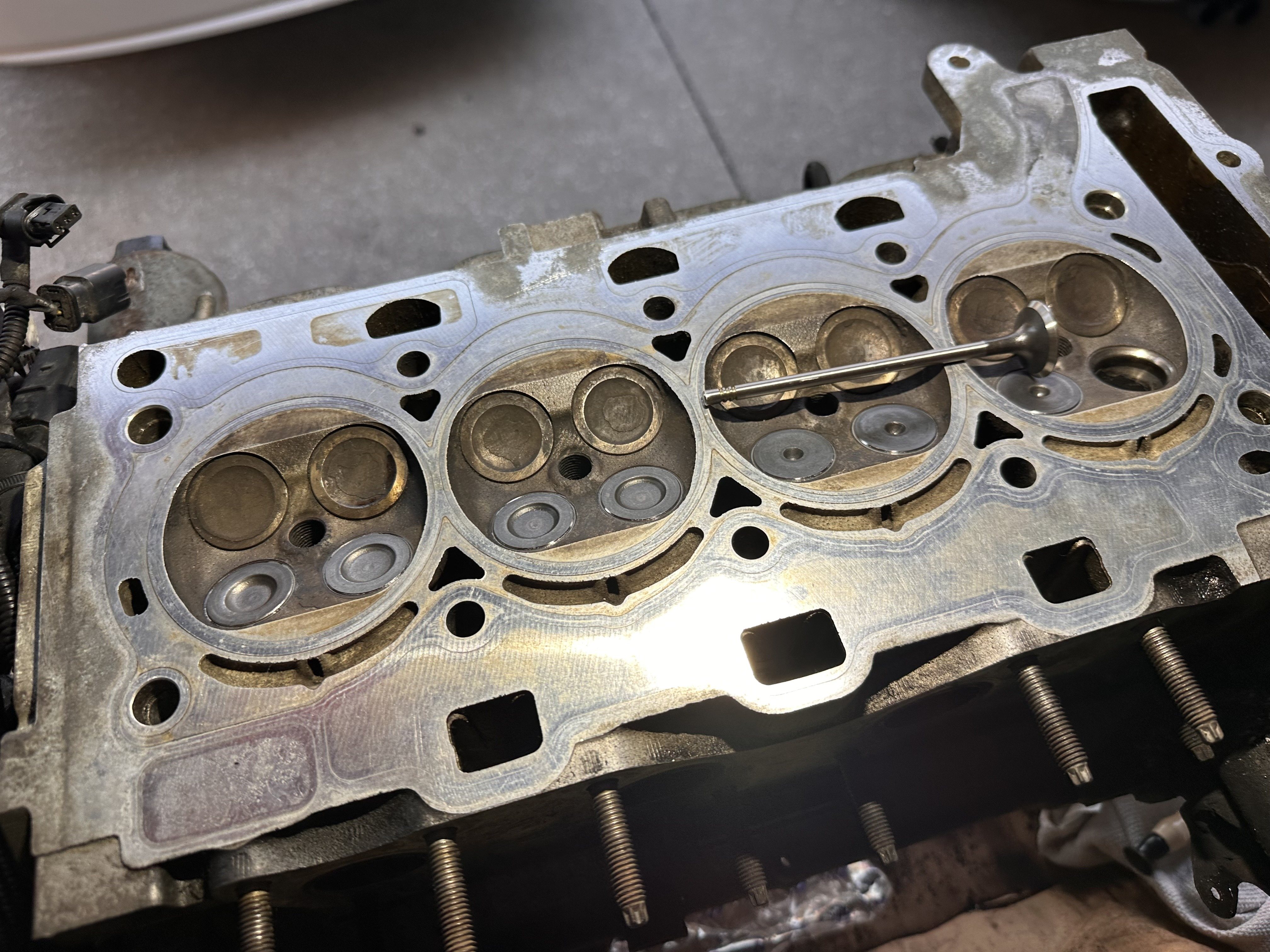 Removed N16 cylinder head on a bench with the combustion chambers facing up and a loose valve resting on the head