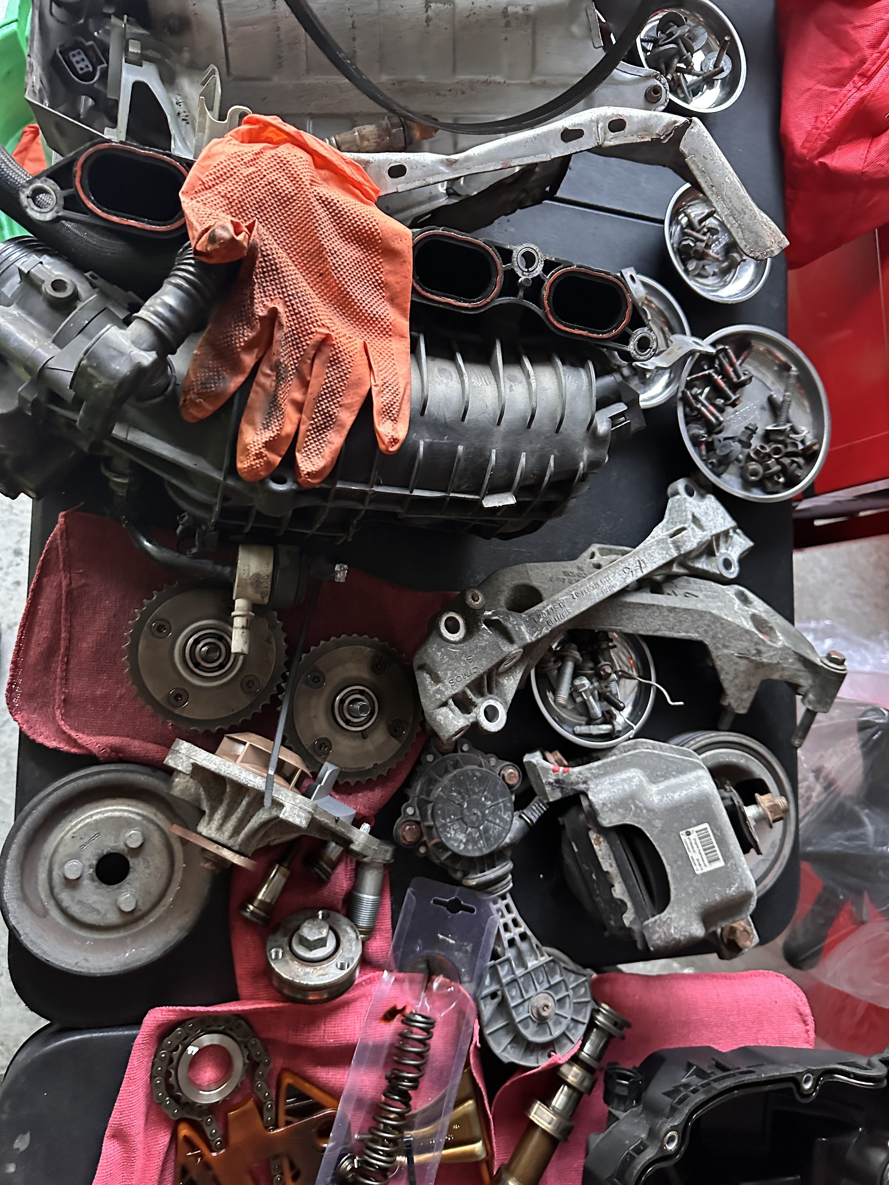 Engine parts removed for cylinder head access laid out on a cardboard sheet, including the intake manifold, camshaft sprockets and timing chain