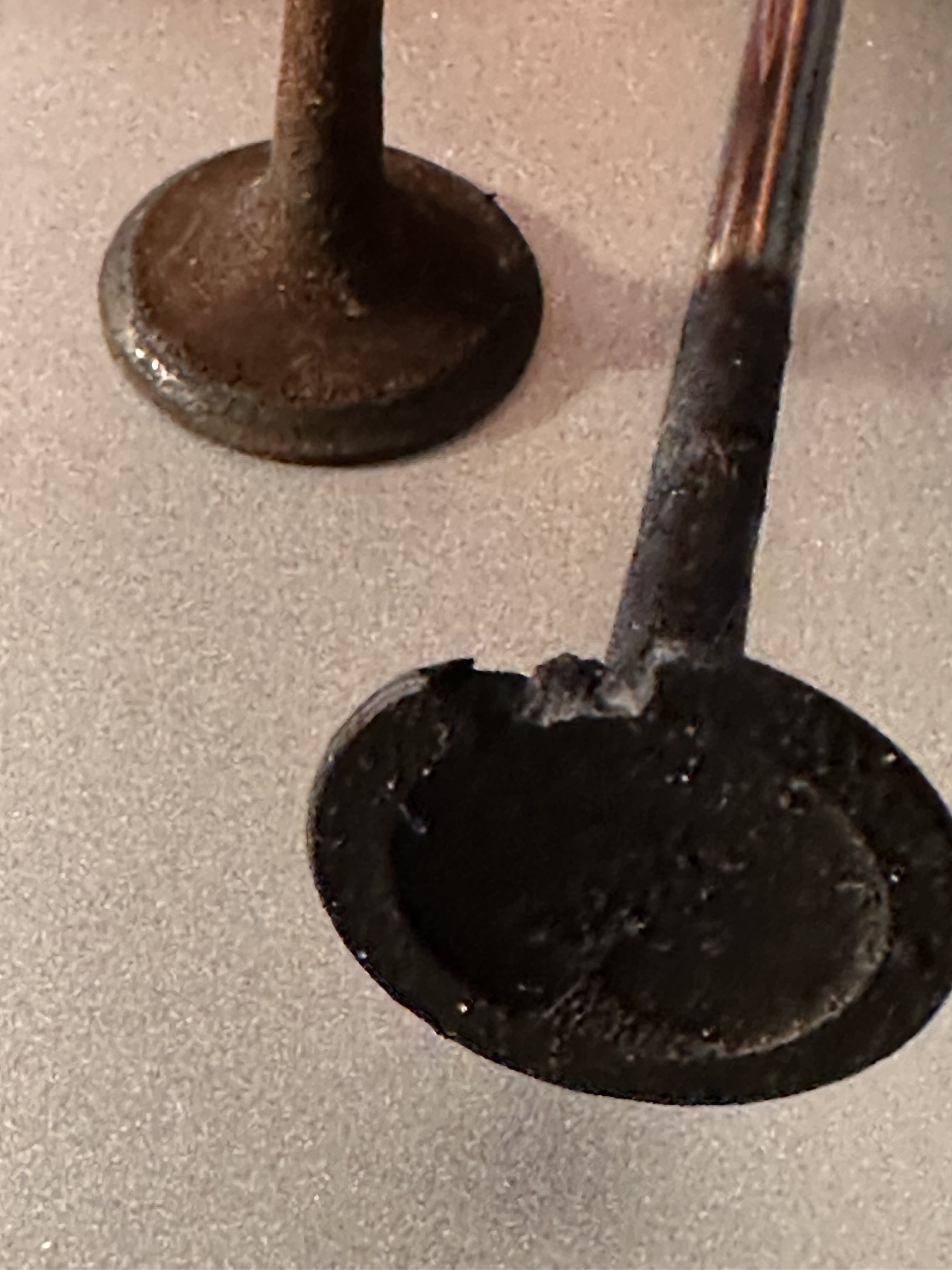 Burned exhaust valve held beside an intact valve, showing the missing section of the valve face