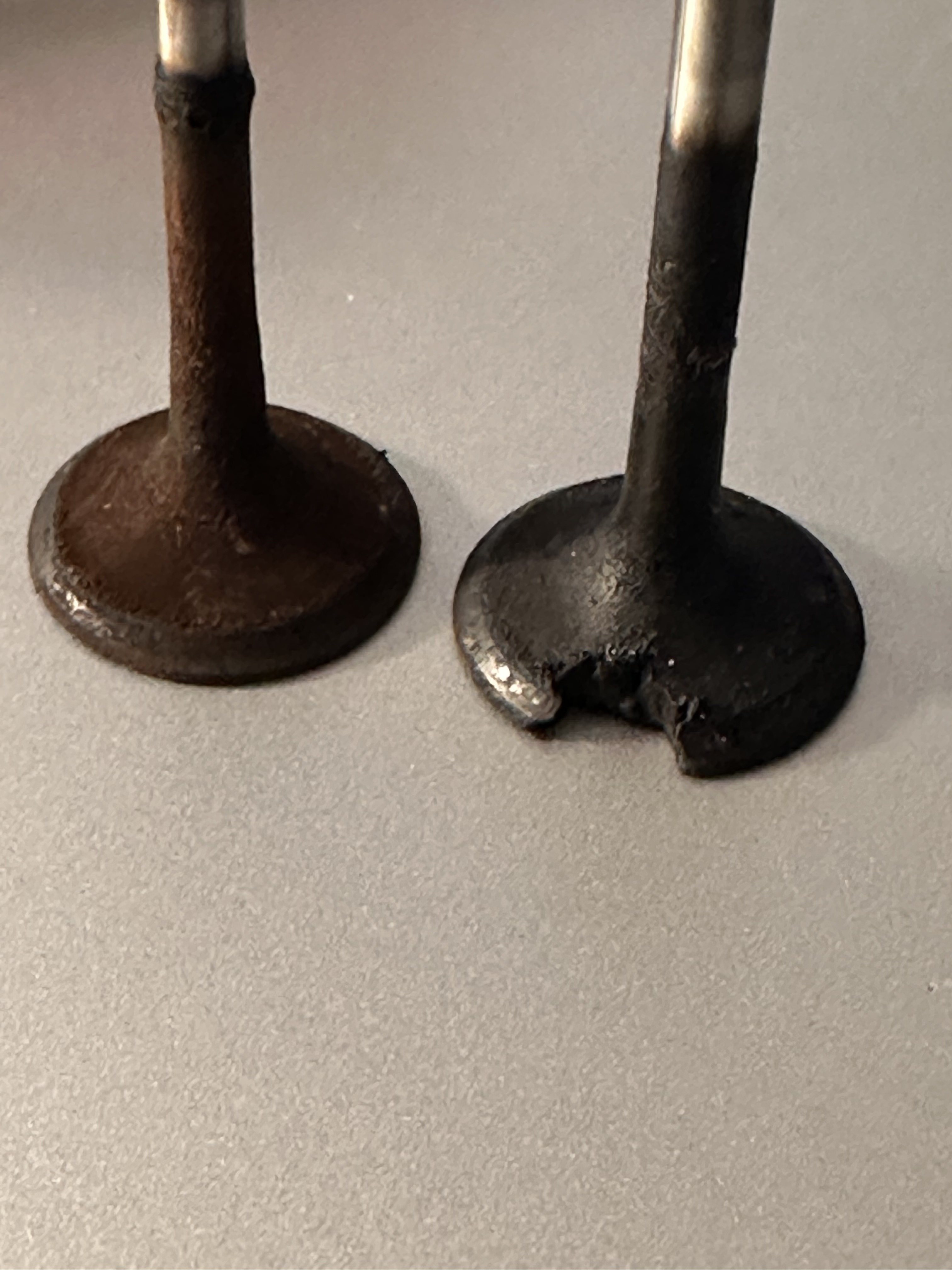 Side view of the burned exhaust valve next to an intact valve, showing the notch in the valve head edge