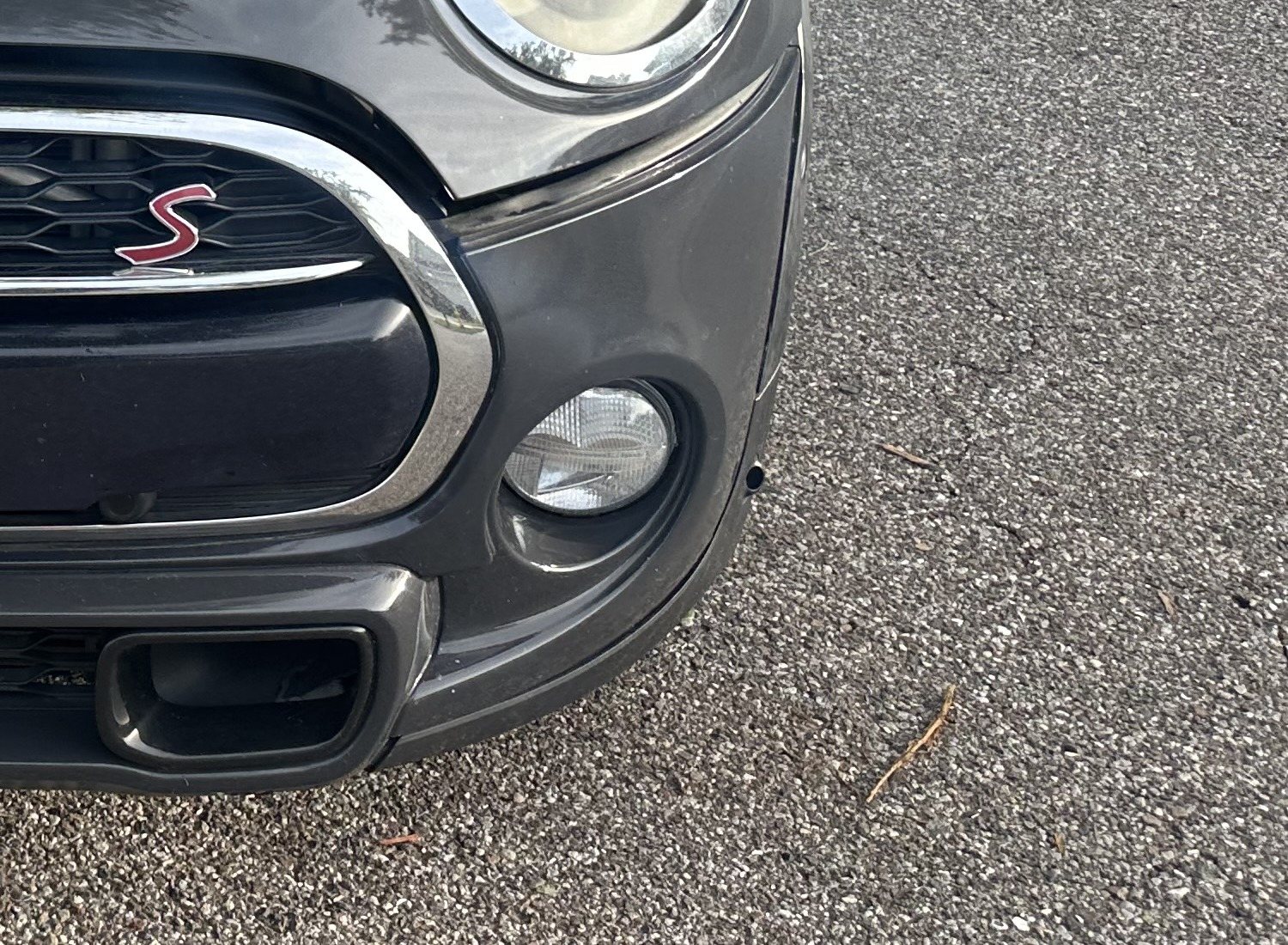 Close-up of the outer left front bumper showing an empty circular opening below the trim line beside the fog lamp