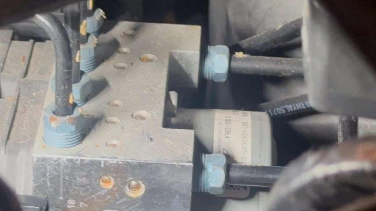 Close-up of an ABS hydraulic block with brake lines threaded into it and a bracket alongside