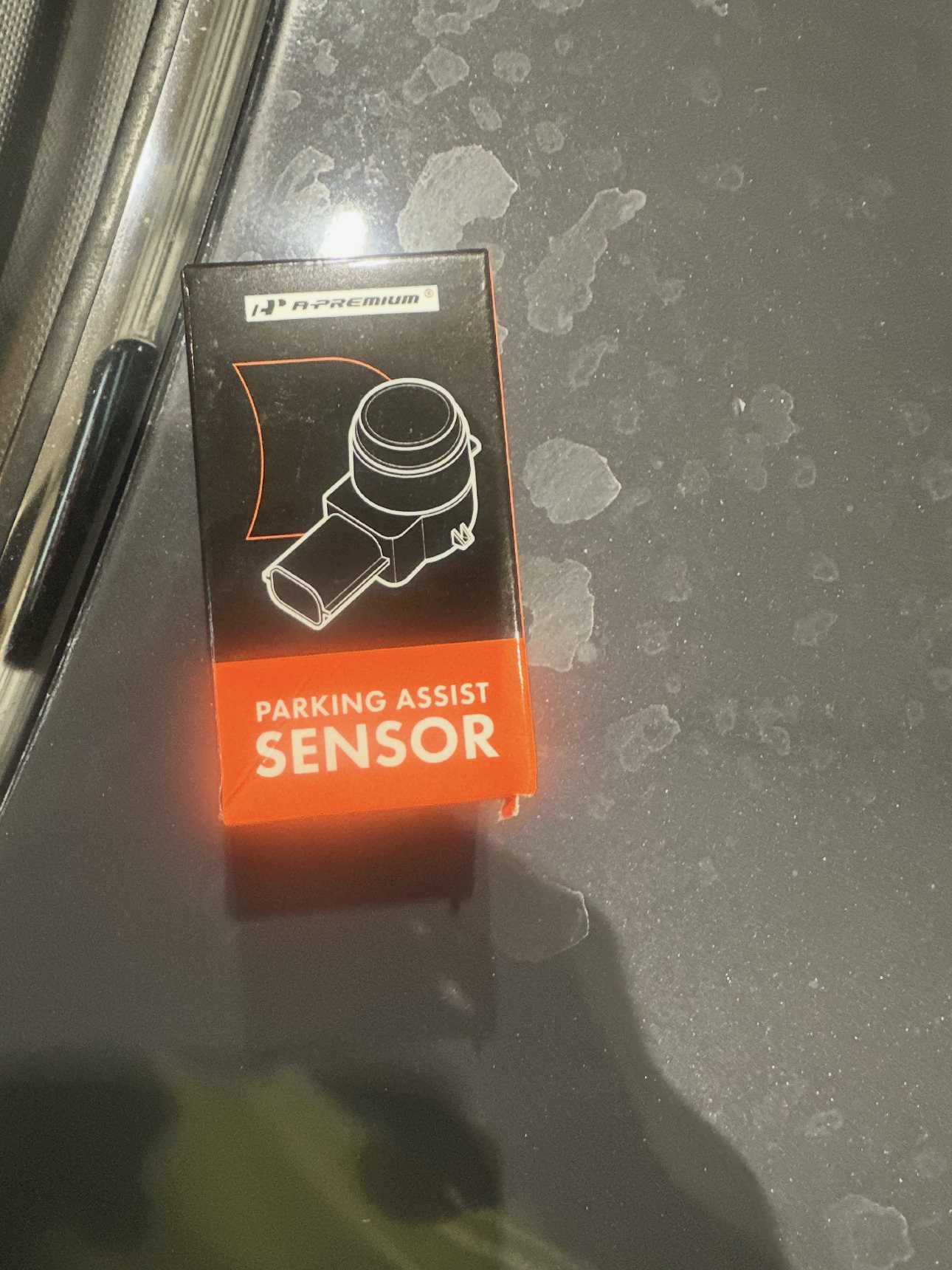 Small retail box labelled Parking Assist Sensor resting on a car bonnet