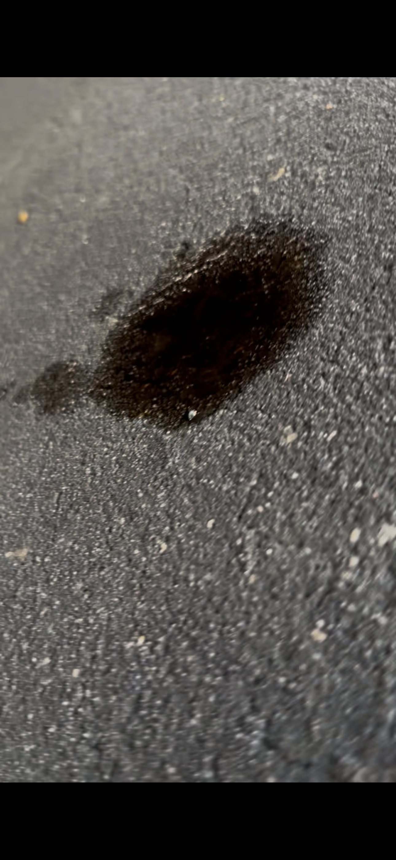 Dark fresh oil spot on asphalt beneath a parked vehicle